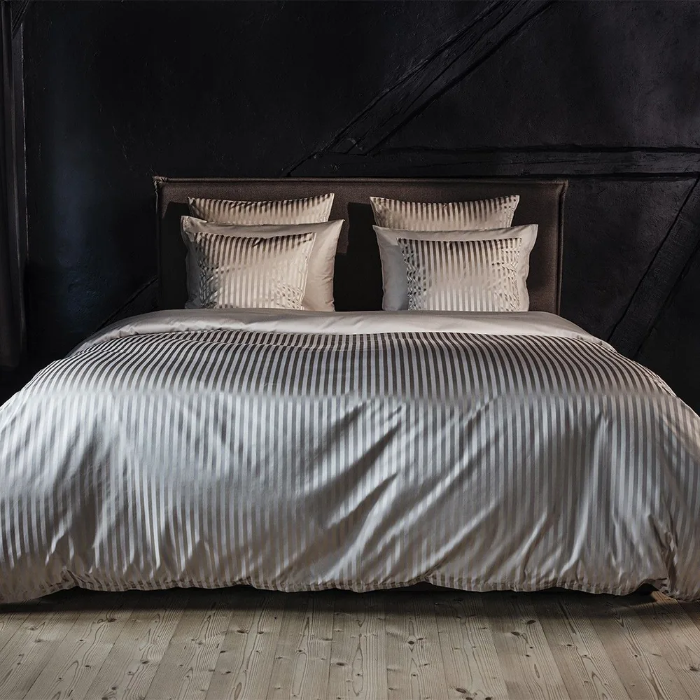 Bed with white, pleated bedding and pillows against a dark wall and wooden floor.