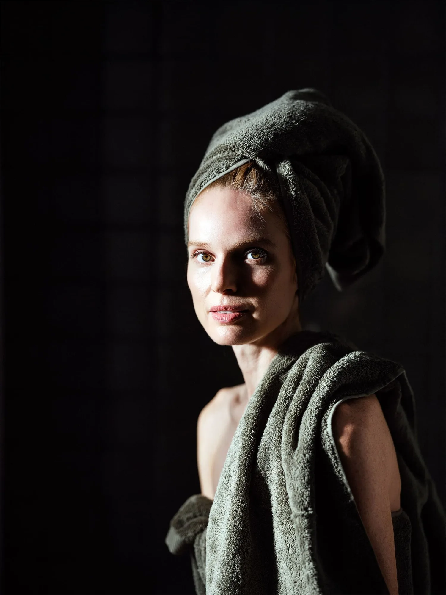 Frau mit Handtuchturban und Frottiertuch von Christian Fischbacher vor dunklem Hintergrund